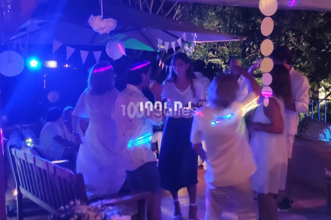 Des personnes dansent sous des lumières colorées lors d'une fête en extérieur, entourées de décorations festives.