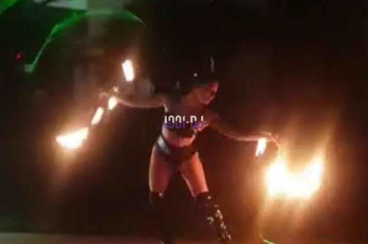 Personne jonglant avec des torches enflammées près d'une piscine, éclairée par des lumières colorées.