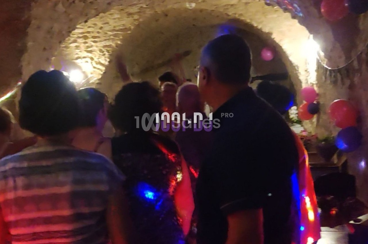 Des personnes dansent dans une cave voûtée éclairée par des lumières colorées et entourée de ballons décoratifs.