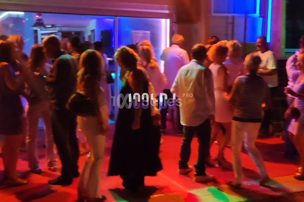 Groupe de personnes dansant et discutant dans un espace éclairé par des lumières colorées en soirée.