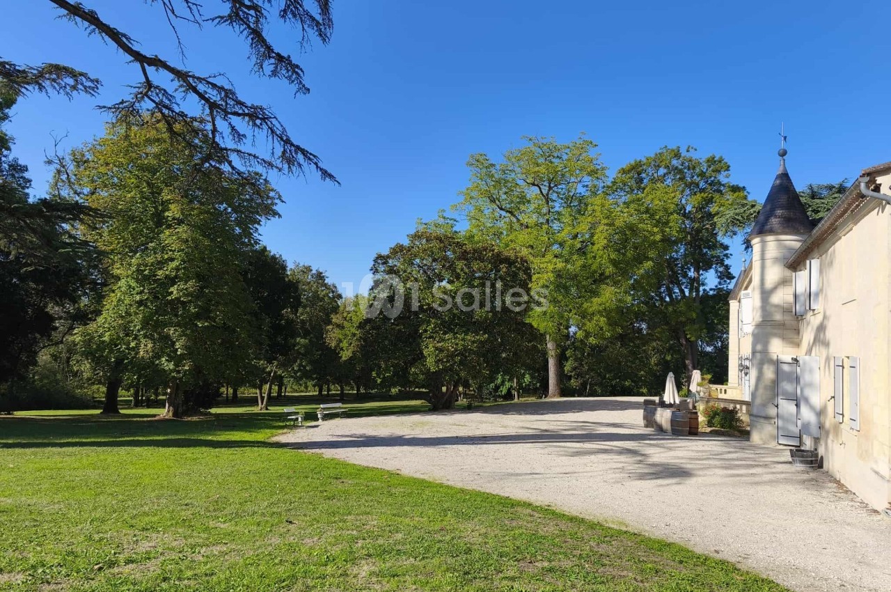Allée gravillonnée bordée d'arbres menant à un bâtiment ancien avec une tourelle, par une journée ensoleillée.