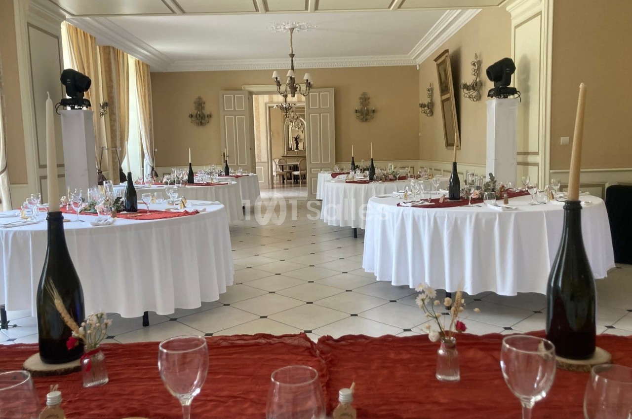 Salle de réception élégante avec tables rondes dressées, nappes blanches et décorations raffinées.