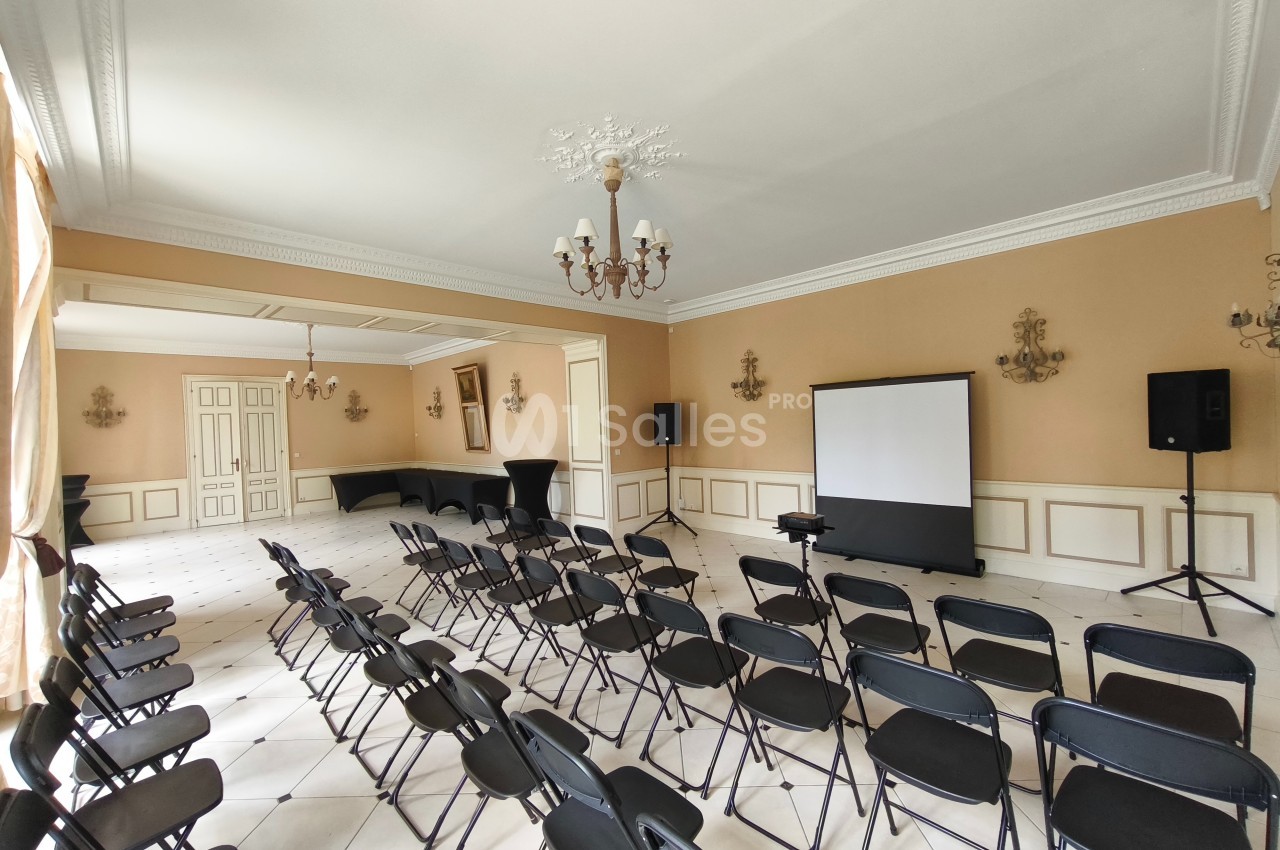 Salle de conférence lumineuse avec chaises noires alignées, écran de projection et équipements audio.