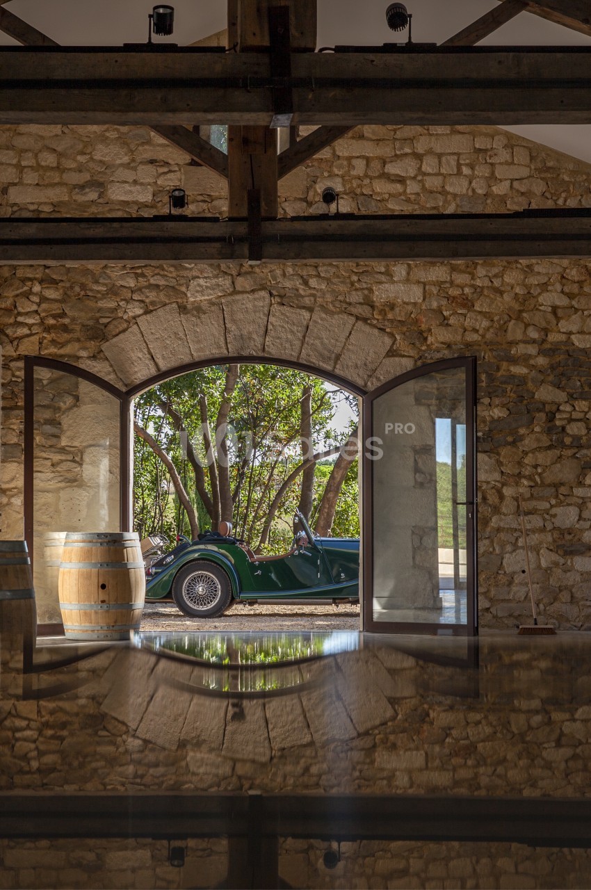 Voiture ancienne verte garée devant une porte voûtée ouverte, dans un bâtiment en pierre avec tonneaux en bois.