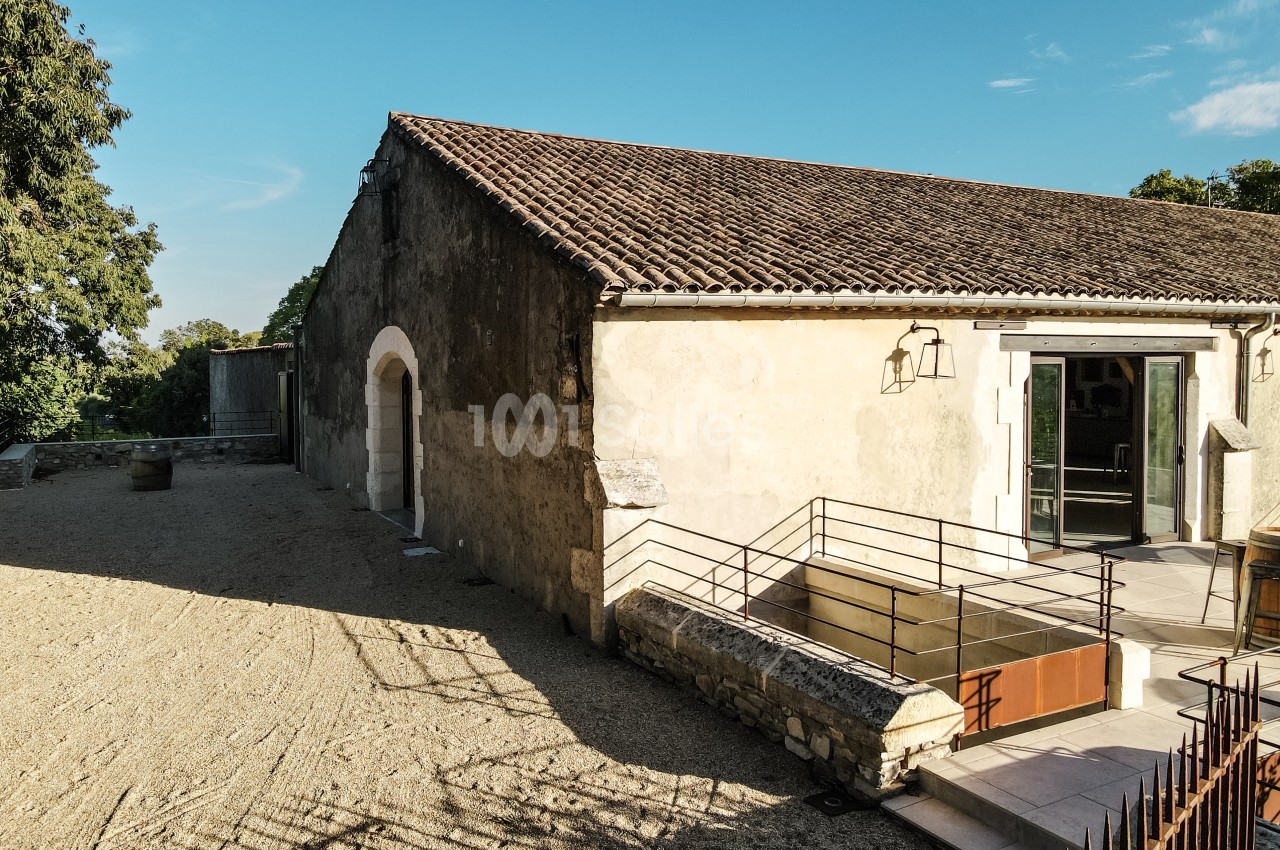 Bâtiment ancien en pierre avec toit en tuiles, rampe d'accès et porte ouverte sous un ciel dégagé.