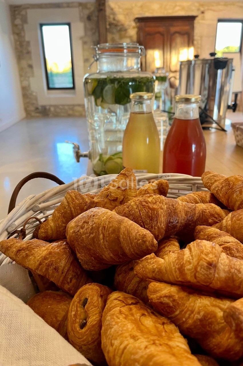 Panier de croissants frais au premier plan, avec des boissons et un grand bocal d'eau infusée en arrière-plan.