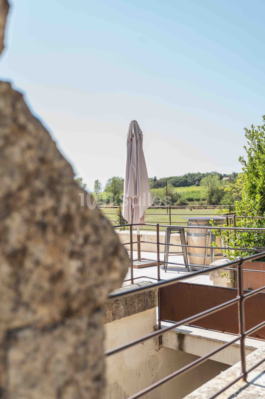 Terrasse extérieure avec parasol fermé, chaises et vue sur les champs verdoyants.