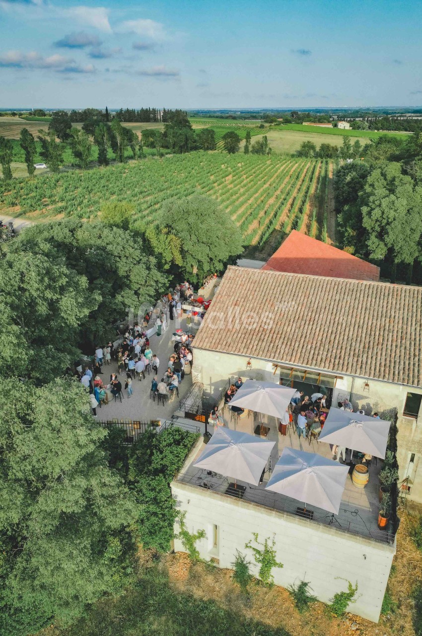 Vue aérienne d'un domaine viticole avec bâtiment en pierre, terrasses ombragées et vignobles environnants.
