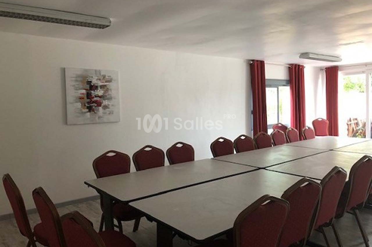 Salle de réunion lumineuse avec une grande table rectangulaire entourée de chaises rouges et un tableau décoratif au mur.