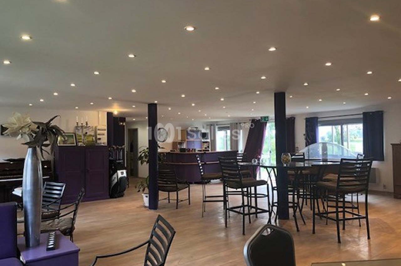 Salle lumineuse avec des tables et chaises en métal, décorée de plantes et éclairée par des spots au plafond.