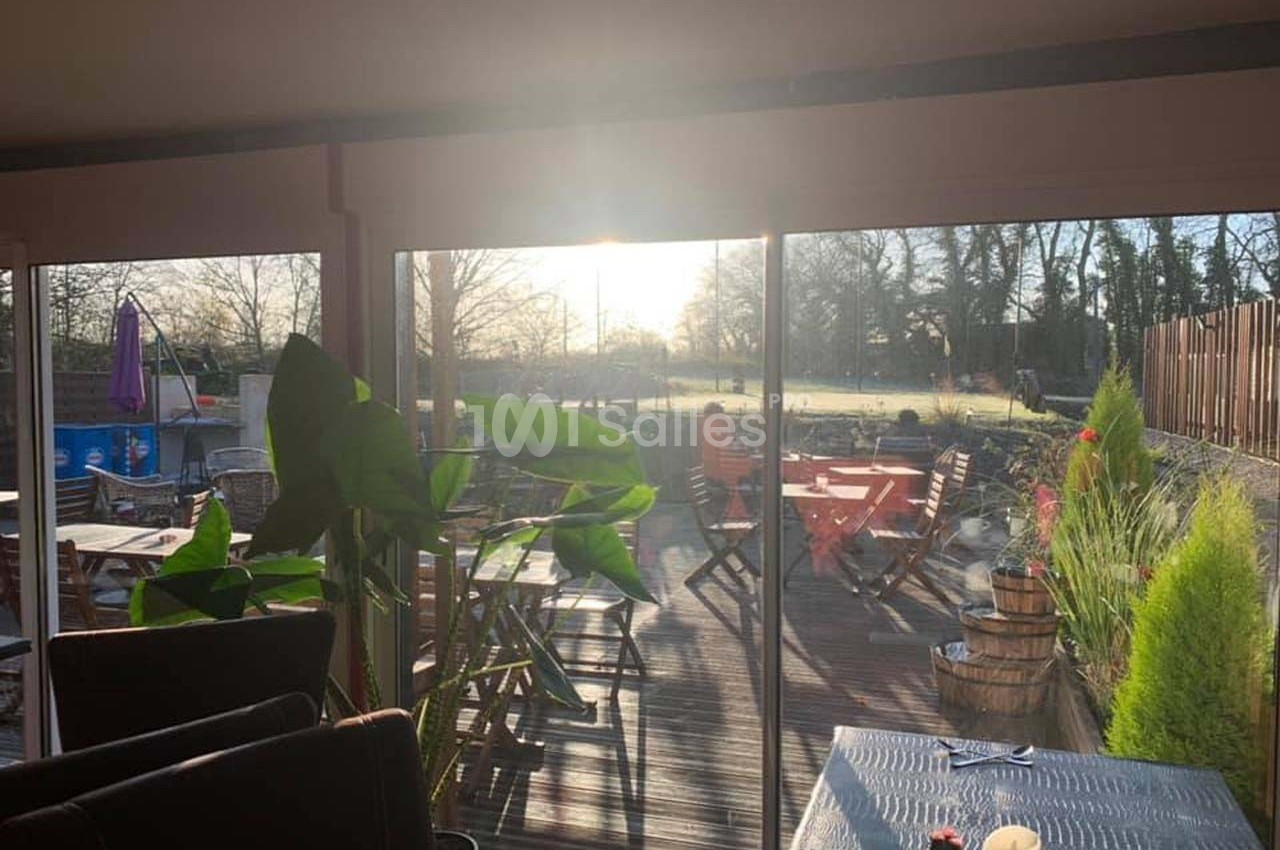 Salle lumineuse avec vue sur une terrasse en bois aménagée, baignée par la lumière du soleil couchant.