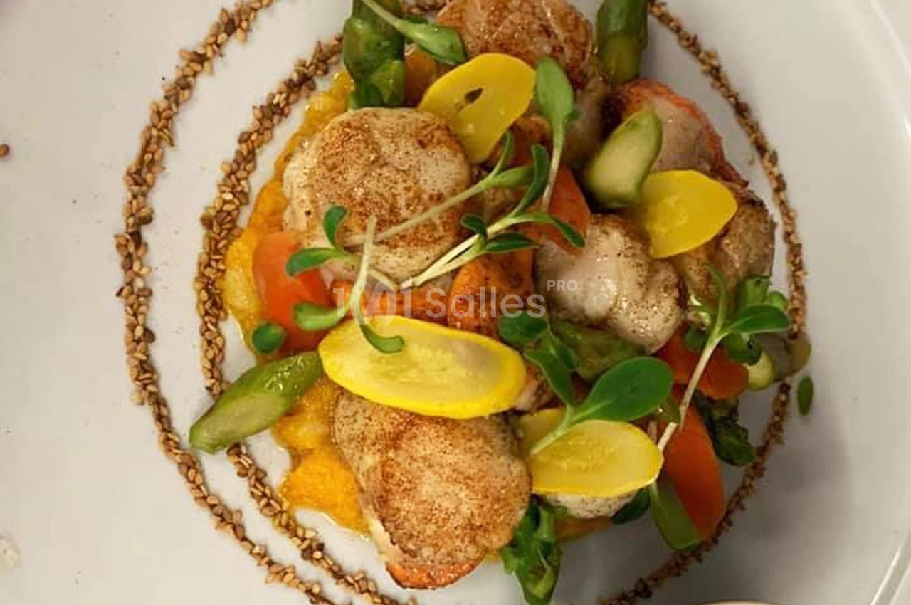 Assiette de noix de Saint-Jacques servies sur un lit de purée, accompagnées de légumes colorés et de jeunes pousses.