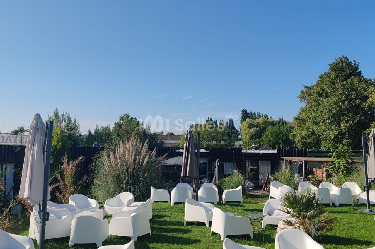 Chaises blanches et parasols disposés sur une pelouse, entourés de végétation et sous un ciel dégagé.