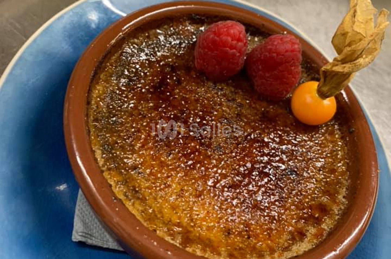 Crème brûlée dorée servie dans un ramequin, décorée de framboises et d'un physalis sur une assiette bleue.