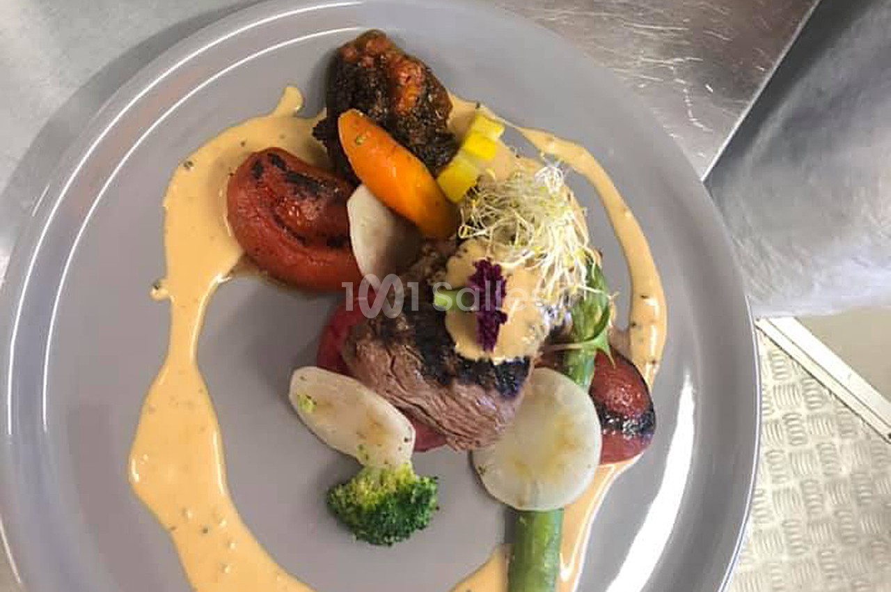 Assiette de viande grillée accompagnée de légumes variés, sauce crémeuse et décoration de pousses germées.