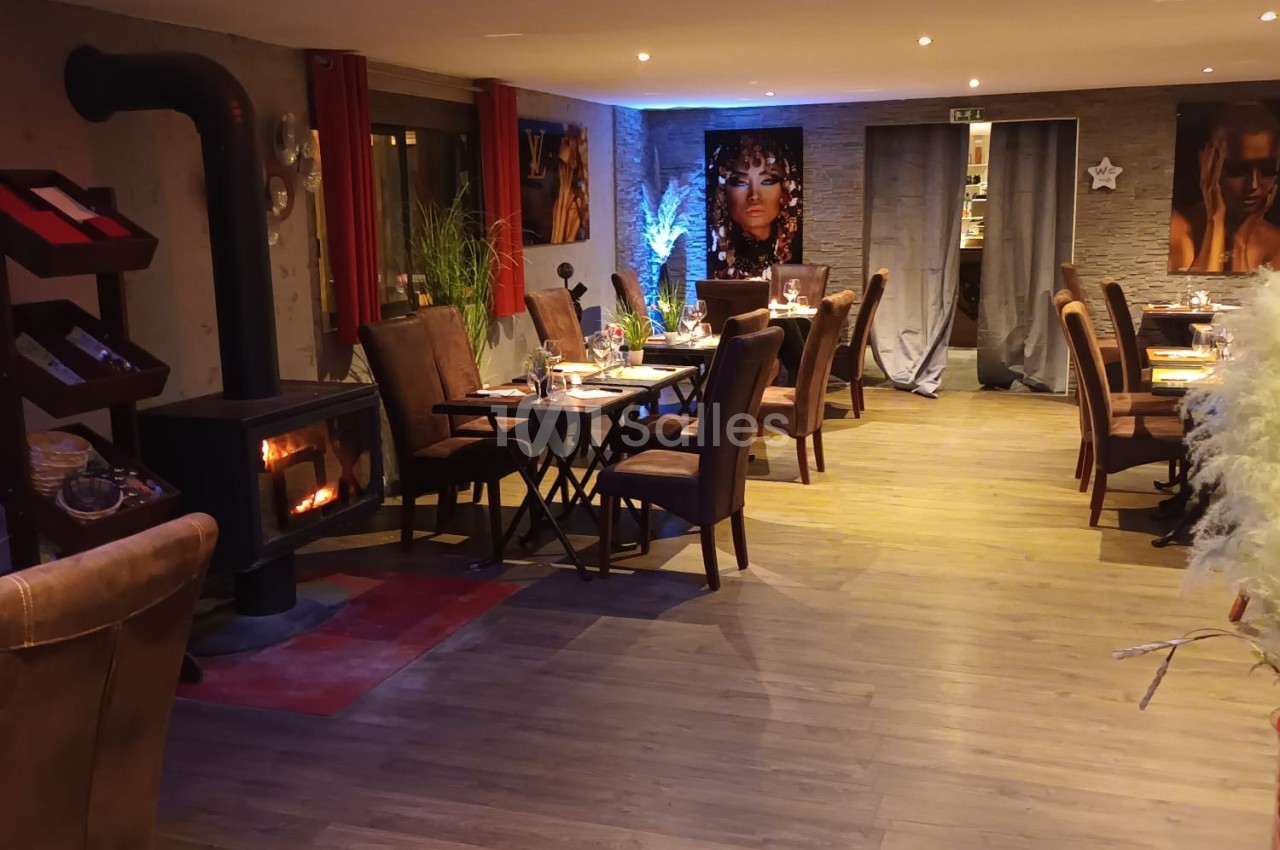 Salle de restaurant chaleureuse avec poêle à bois, tables dressées, décorations et éclairage tamisé.