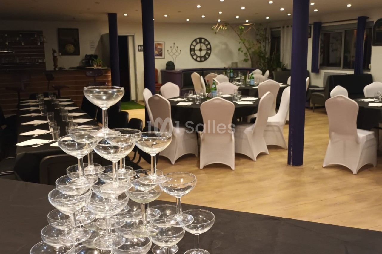 Salle de réception décorée avec des tables dressées et une pyramide de coupes à champagne au premier plan.