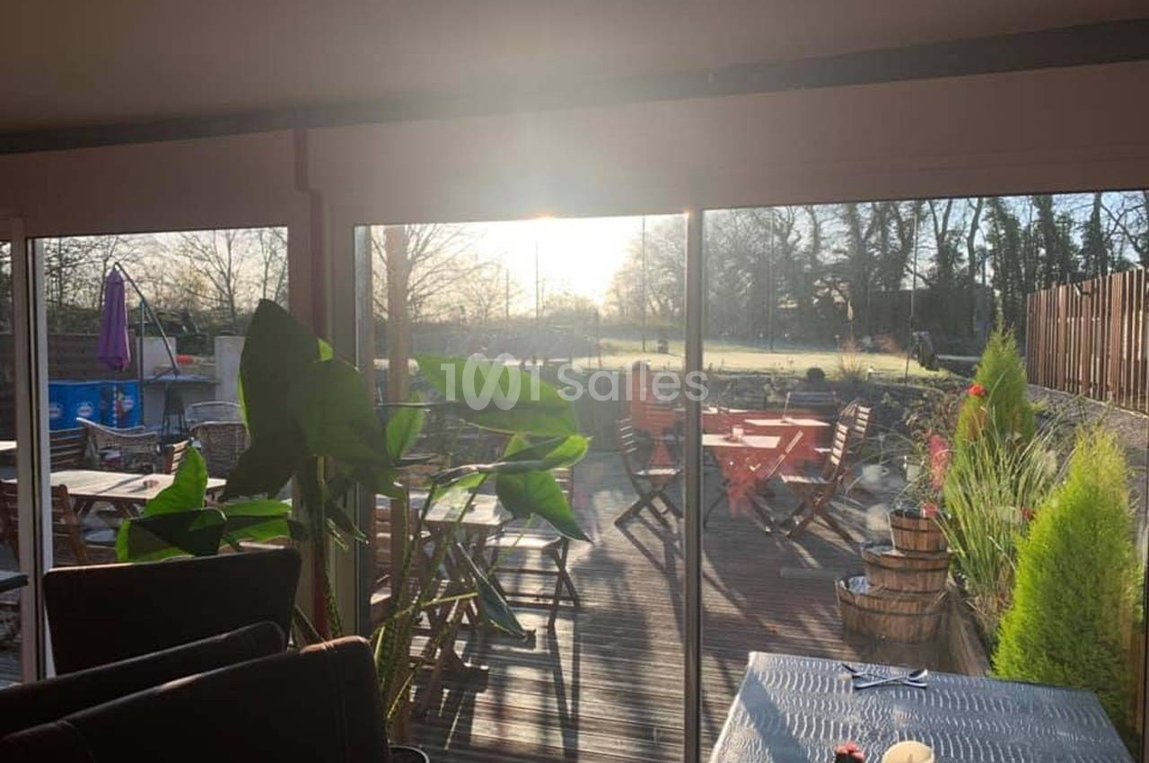 Salle lumineuse avec vue sur une terrasse en bois aménagée, baignée par la lumière du soleil couchant.