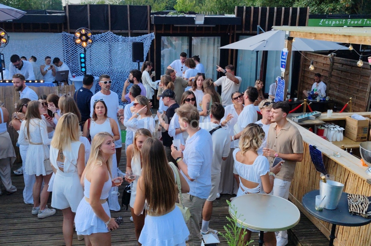 Groupe de personnes en tenue estivale blanche réunies sur une terrasse en bois lors d'un événement en plein air.