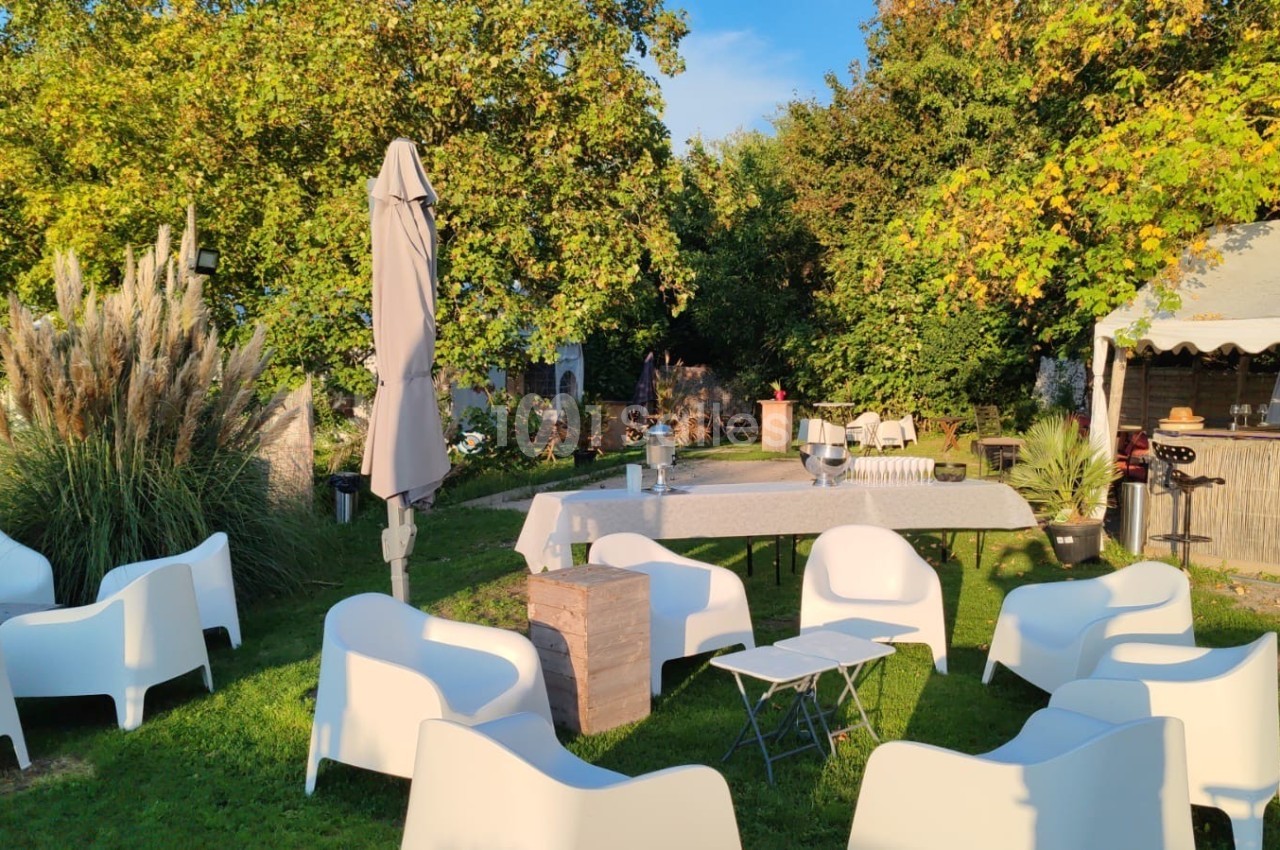 Mobilier de jardin blanc disposé sur une pelouse, avec une table dressée et un stand en bois sous un auvent.