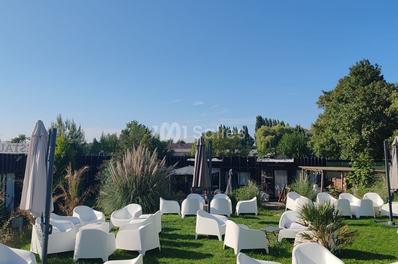 Chaises blanches et parasols disposés sur une pelouse, entourés de végétation et sous un ciel dégagé.
