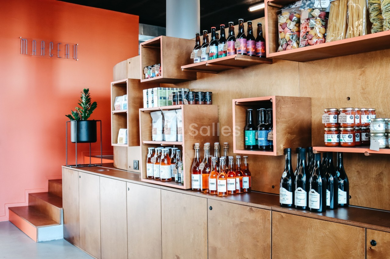 Étagères en bois avec bouteilles, bocaux, et produits alimentaires exposés dans un espace au mur orange.
