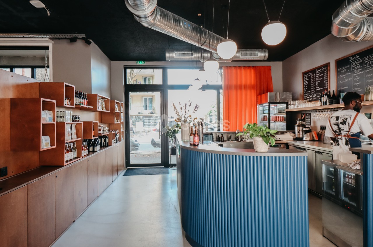 Intérieur d'un café moderne avec comptoir bleu, étagères en bois, éclairage suspendu et grande baie vitrée.