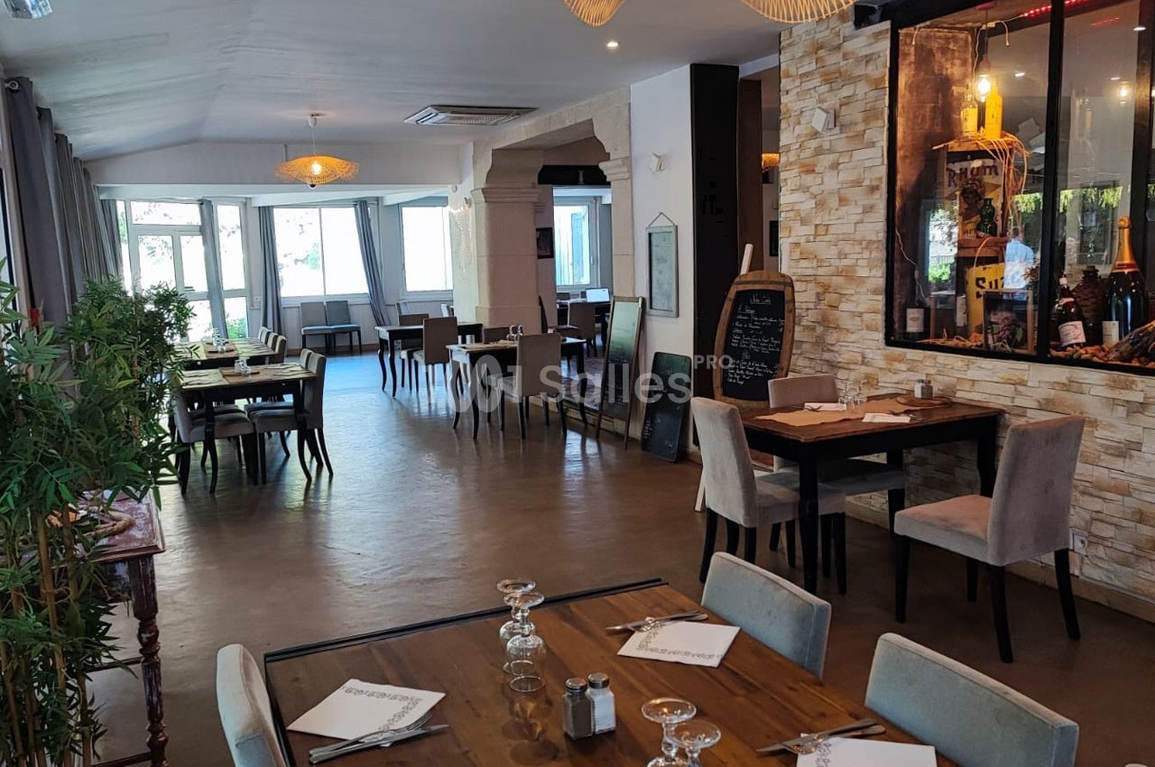 Salle de restaurant lumineuse avec tables dressées, décoration moderne et murs en pierre apparente.