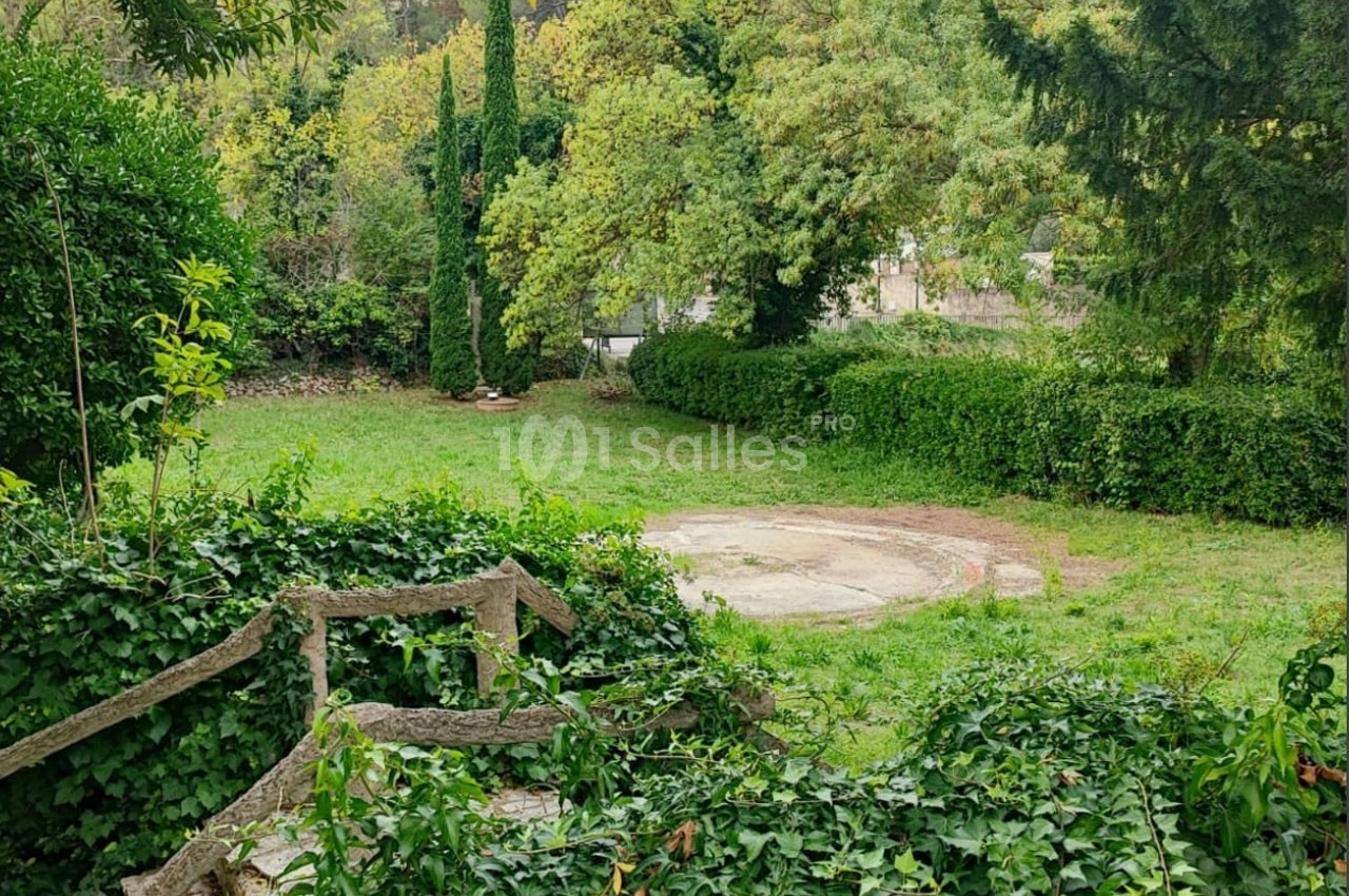 Jardin verdoyant avec pelouse, arbres et buissons, entourant une petite clairière circulaire en béton.