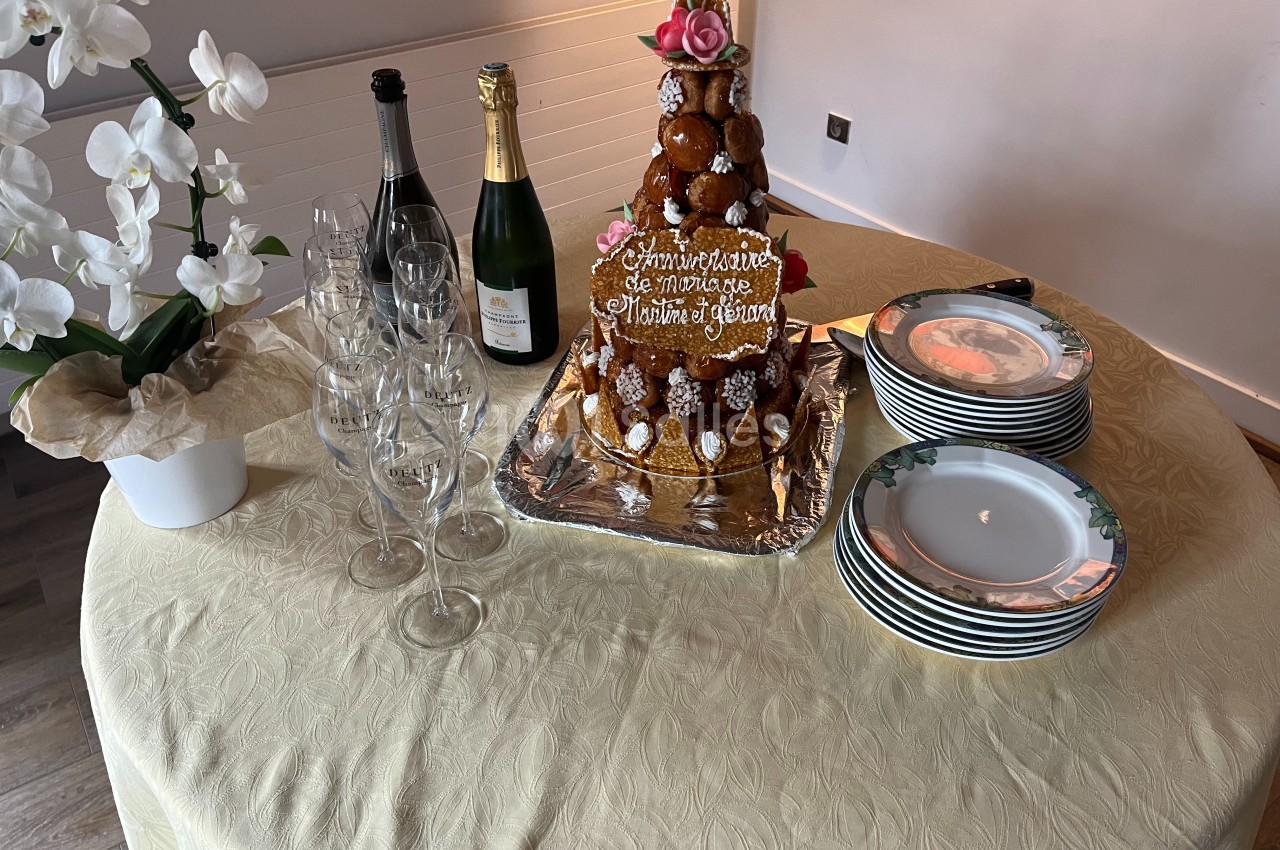 Pièce montée de choux décorée de roses avec des bouteilles de champagne, flûtes et assiettes sur une table dressée.