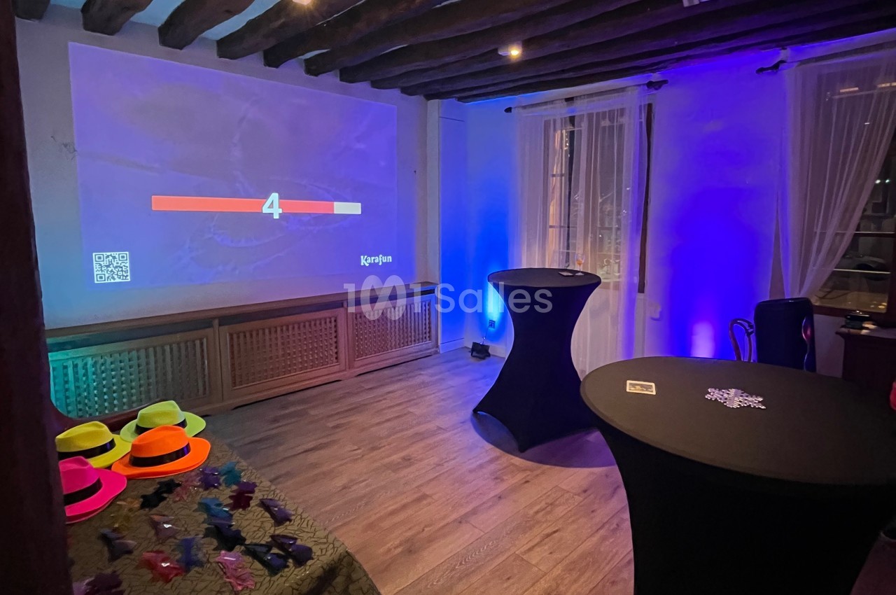 Salle éclairée avec des lumières colorées, équipée d'un écran projetant un compte à rebours et de tables décorées.