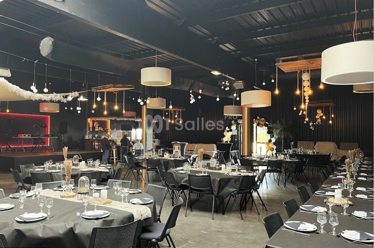 Salle de réception décorée avec des tables dressées, des guirlandes lumineuses et un bar en arrière-plan.