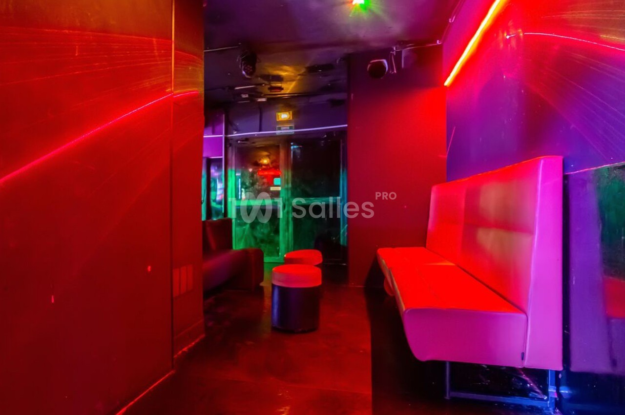 Salle avec éclairage néon rouge et violet, banquettes et tabourets noirs, ambiance de bar ou club nocturne.