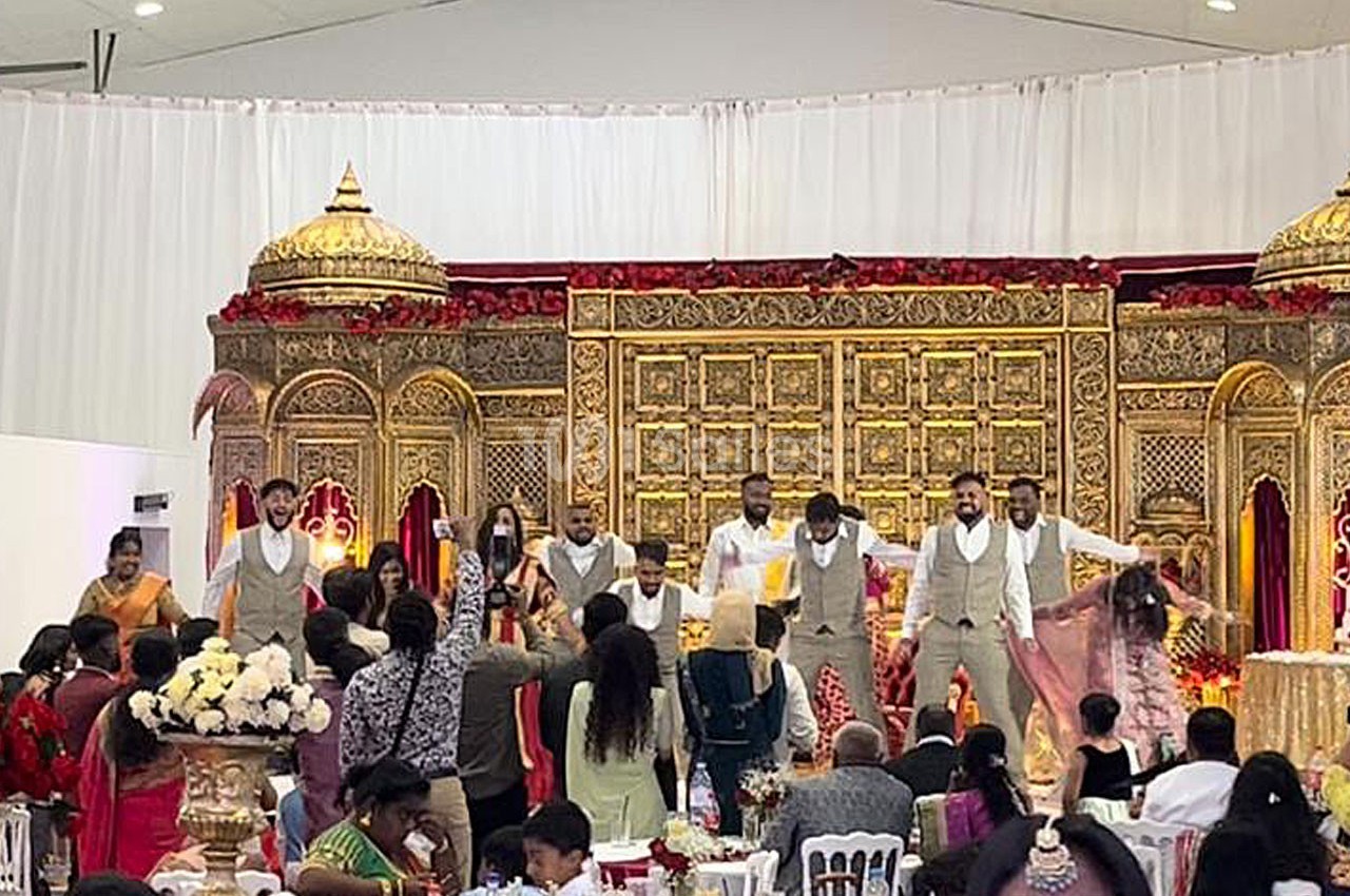 Des invités assistent à une danse festive sur une scène ornée de décorations dorées lors d'une célébration.