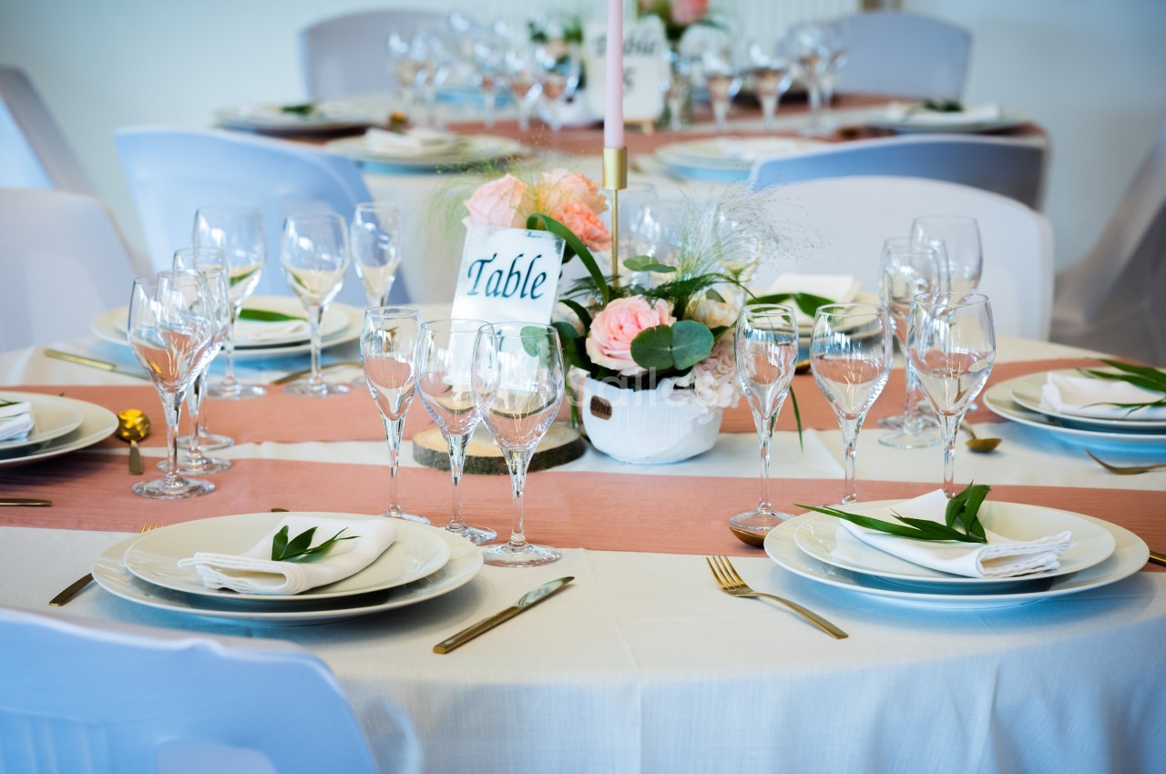 Table dressée avec une nappe blanche, vaisselle élégante, verres à pied et centre de table floral.