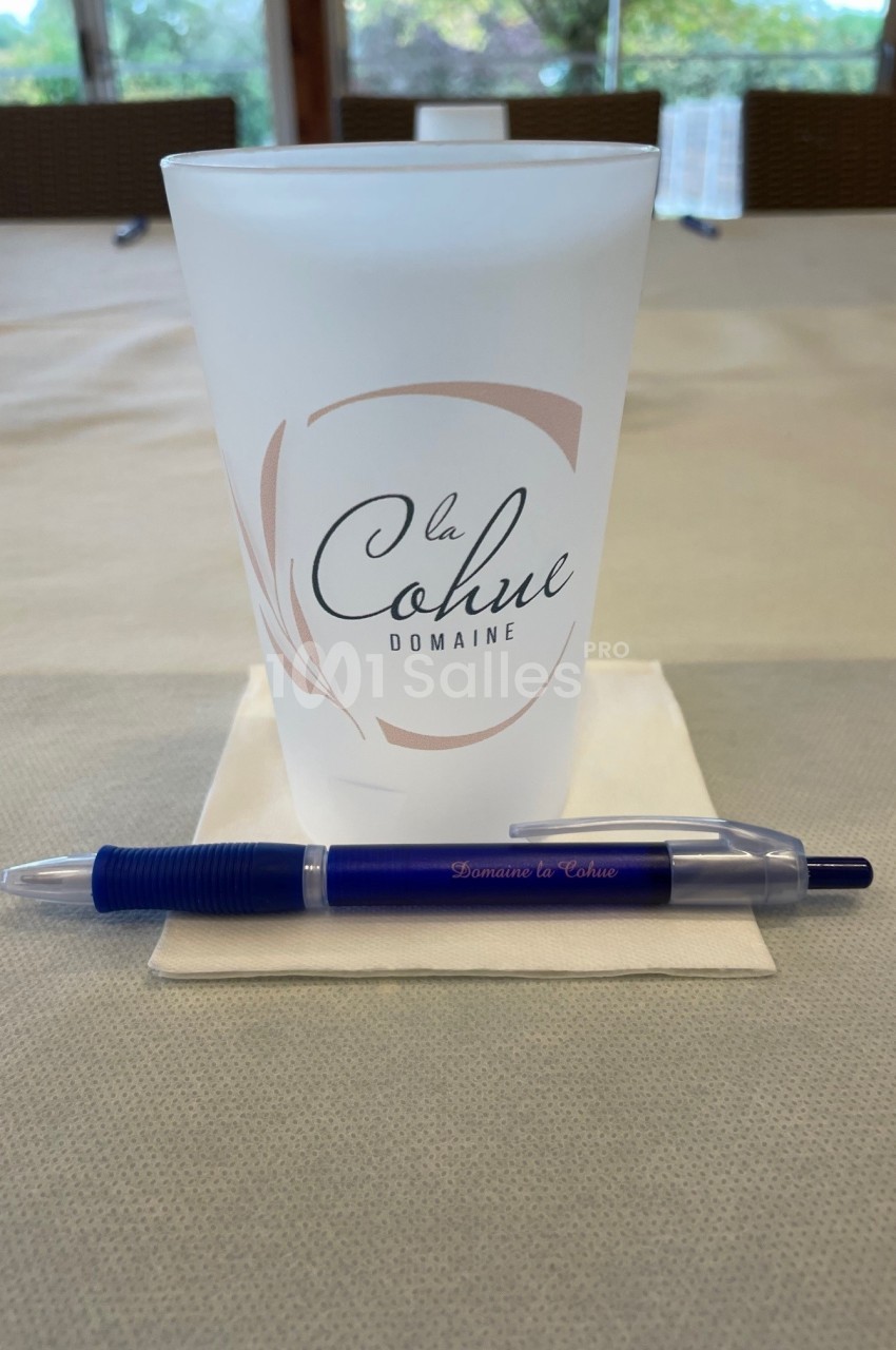 Gobelet réutilisable et stylo bleu posés sur une serviette blanche, sur une table beige.