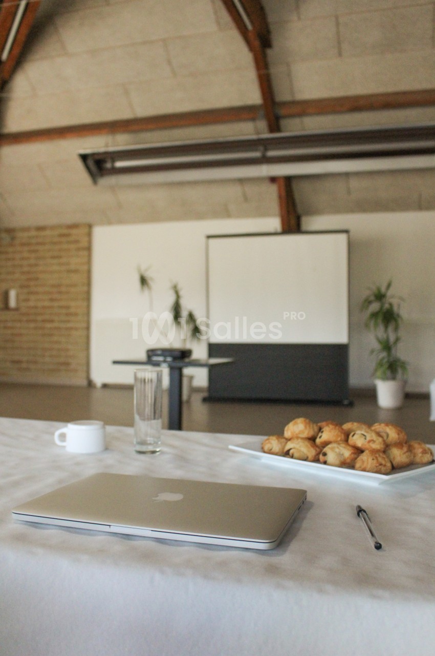 Ordinateur portable, tasse, verre et assiette de viennoiseries sur une table, avec un projecteur en arrière-plan.