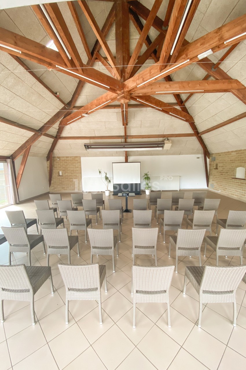 Salle de réunion lumineuse avec des chaises disposées en rangées face à un écran de projection et un tableau blanc.