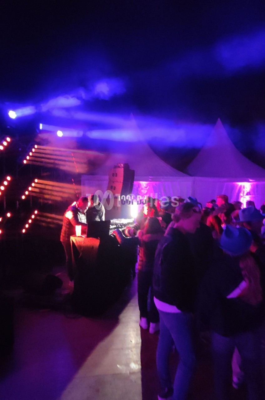 Des personnes dansent devant un DJ sous des lumières colorées lors d'un événement en plein air nocturne.