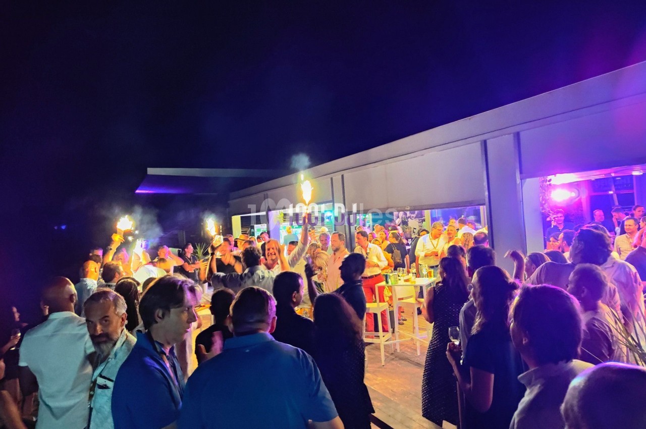 Groupe de personnes rassemblées en soirée festive en extérieur, éclairée par des lumières colorées.