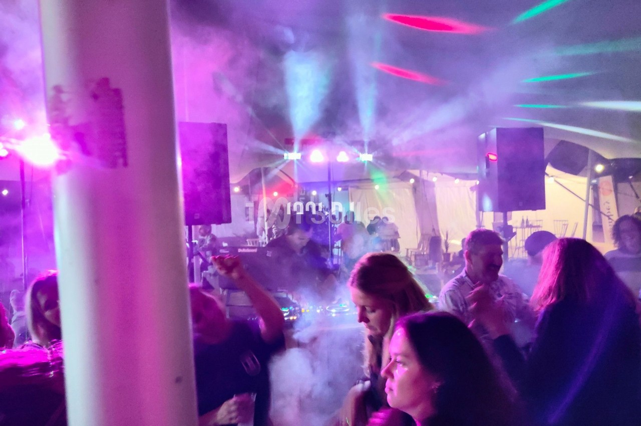 Personnes dansant sous des jeux de lumière colorés et de la fumée dans une ambiance festive en intérieur.