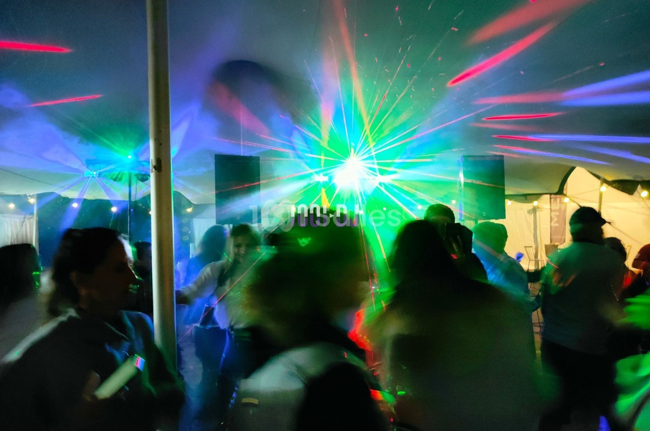 Personnes dansant sous une tente avec des lumières colorées et des effets laser lors d'une soirée festive.