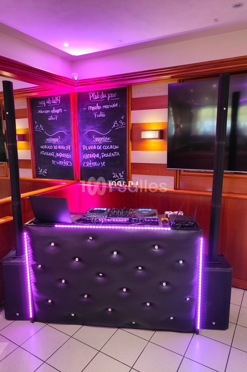 Console de DJ éclairée par des lumières violettes, installée dans un espace intérieur avec des tableaux noirs en arrière…
