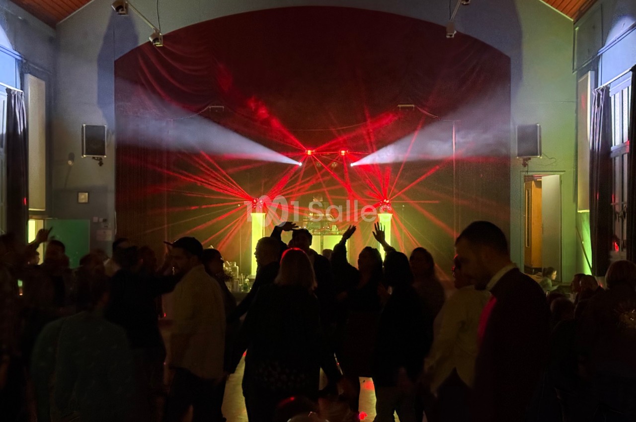 Des personnes dansent dans une salle sombre éclairée par des faisceaux lumineux rouges et jaunes.