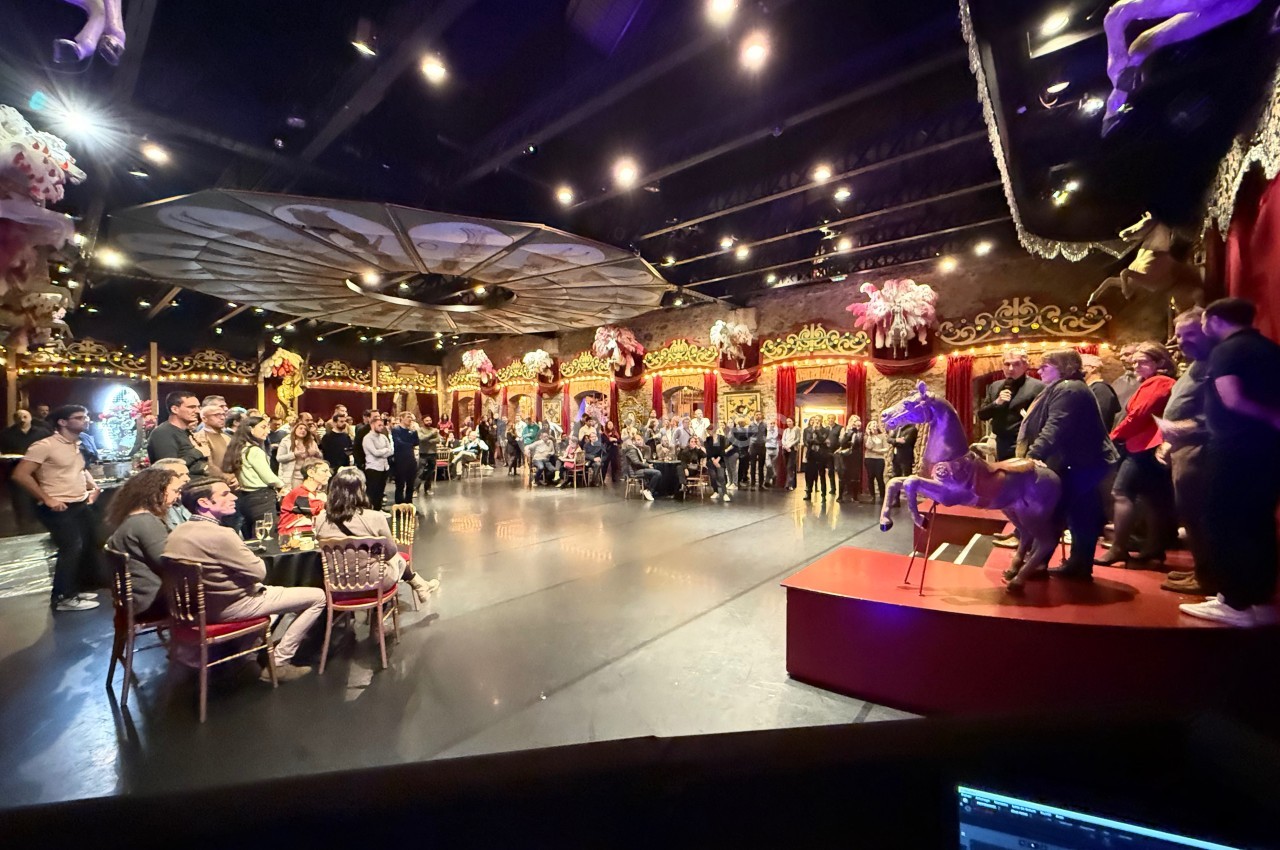 Salle de spectacle avec un public debout et assis, décorations festives et scène éclairée avec une présentation en cours.