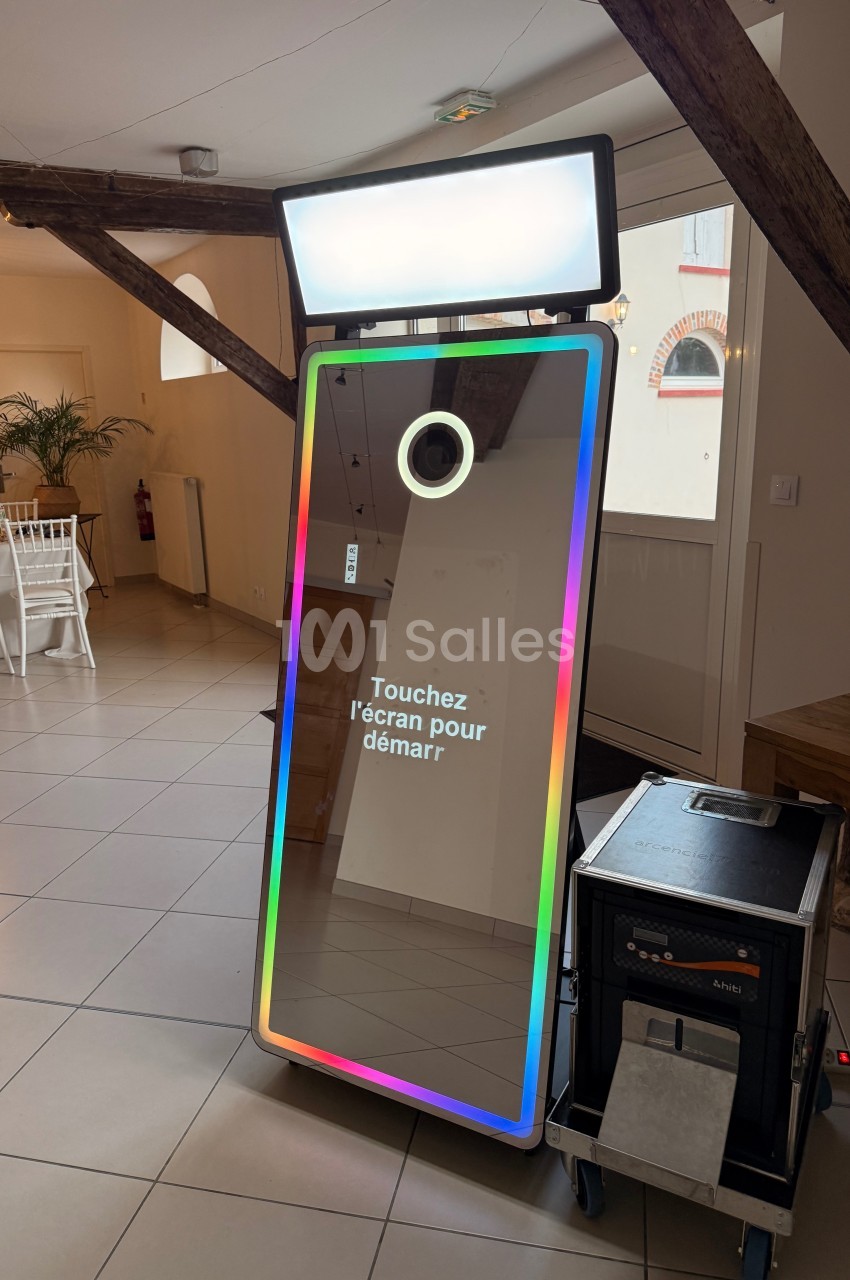 Borne photo interactive avec écran tactile et cadre lumineux, installée dans une salle avec poutres apparentes.