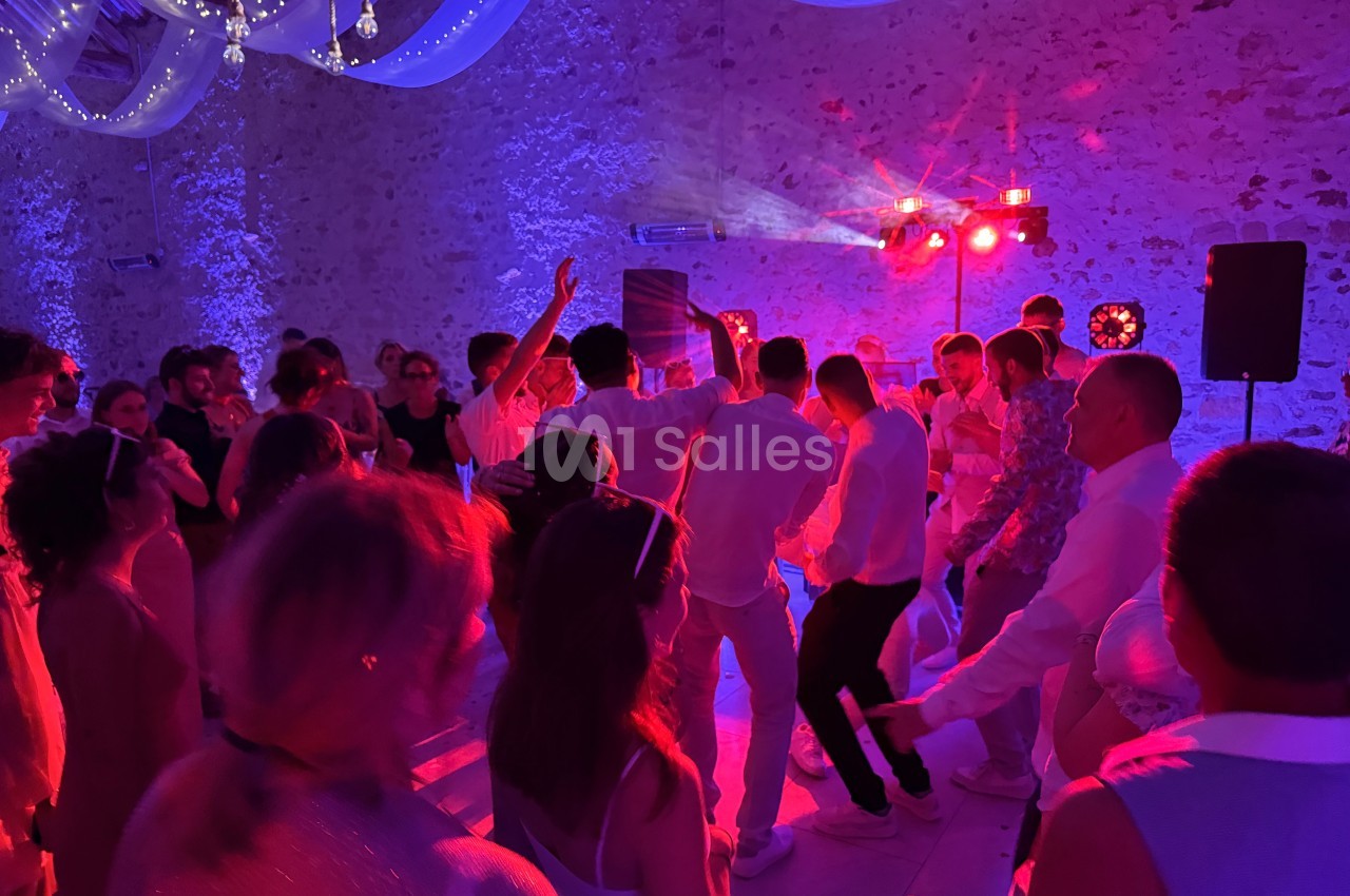 Groupe de personnes dansant sous des lumières colorées dans une salle en pierre décorée de voilages suspendus.
