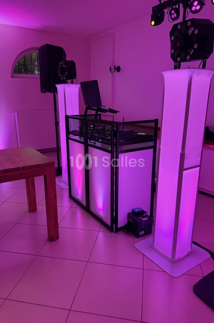 Installation de matériel de DJ avec éclairage LED rose dans une salle au sol carrelé et murs clairs.