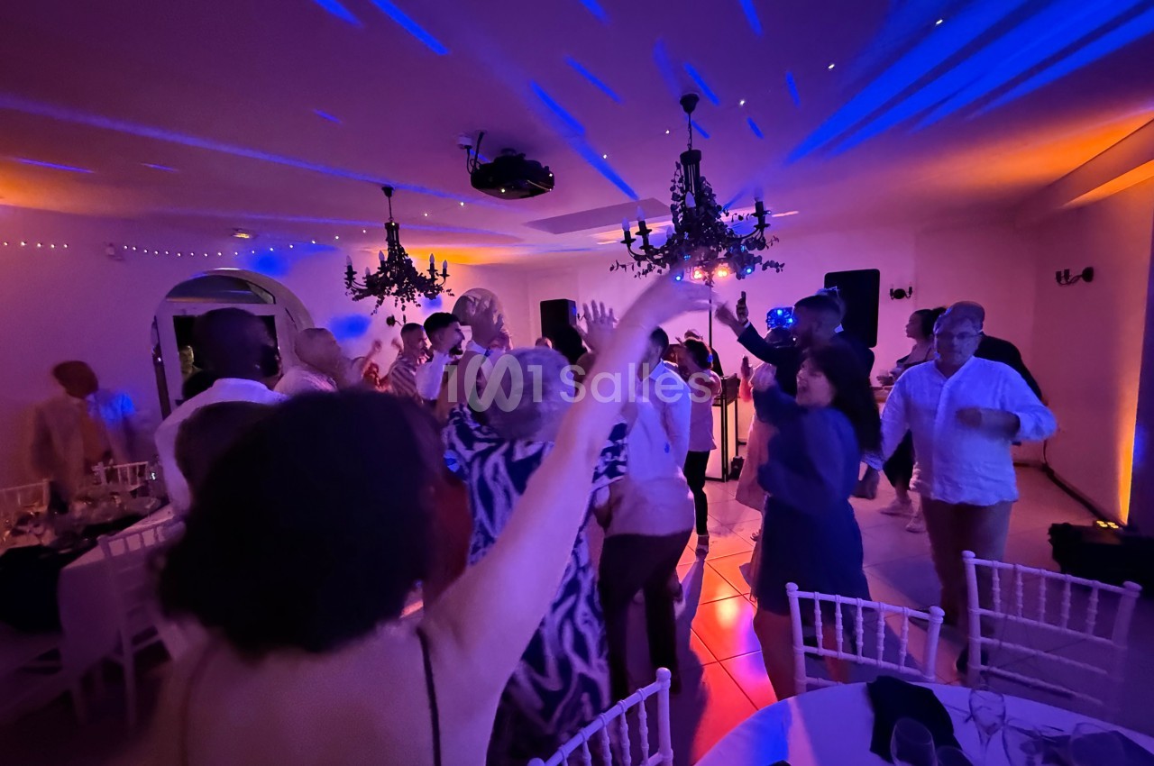 Des personnes dansent sous des lumières colorées dans une salle décorée avec des chandeliers suspendus.