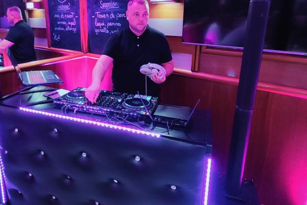 Un DJ mixe de la musique sur une console éclairée par des lumières violettes dans un espace intérieur.